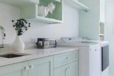 a lovely mint green kitchen with shaker cabinets and open ones, white stone countertops and white appliances