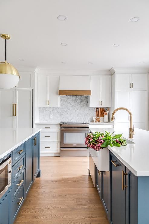 a lovely modern farmhouse kitchen with white upper and egg blue lower cabinets, white stone countertops and pendant lamps