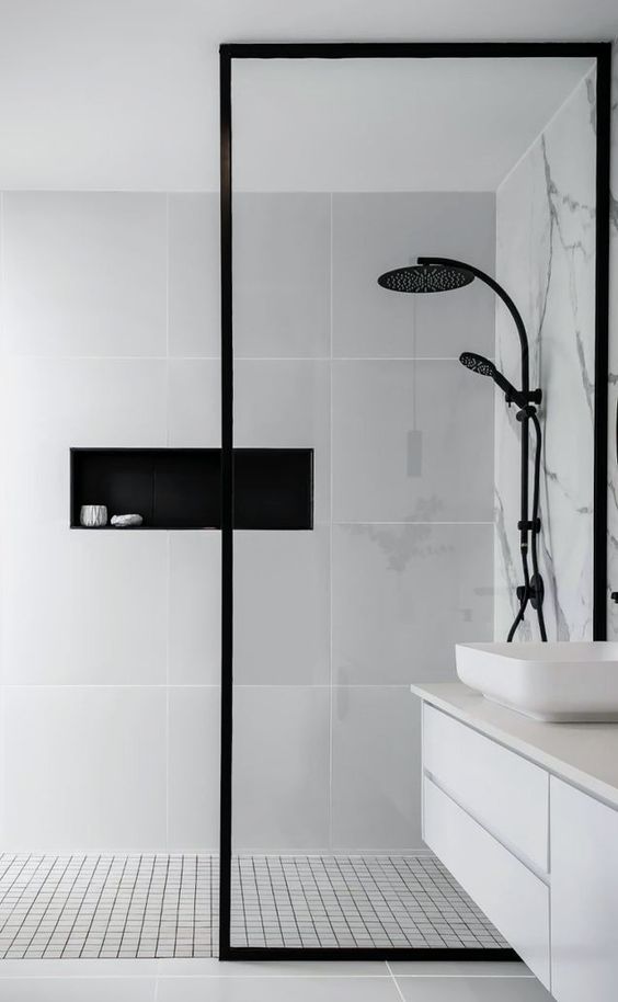a minimalist bathroom with a marble wall, large format grey tiles and smaller ones, a white vanity and black fixtures
