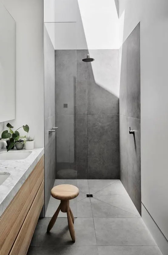 a minimalist bathroom with a shower with large scale tiles and a skylight, a timber vanity, a wooden stool and a mirror