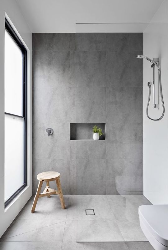 a minimalist bathroom with large scale concrete tiles, white appliances, a wooden stool and a window with non-sheer glass