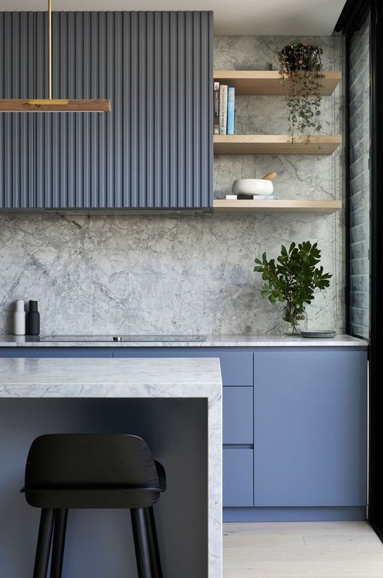 a minimalist blue kitchen with a grey stone backsplash and countertops plus potted greenery and touches of gold