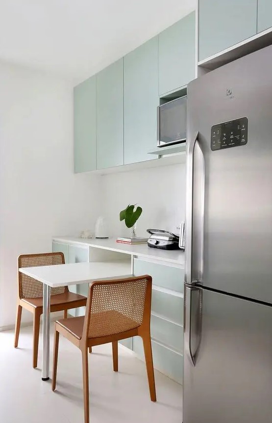a minimalist mint flat panel kitchen with a white stone backsplash and countertops and stainless steel touches
