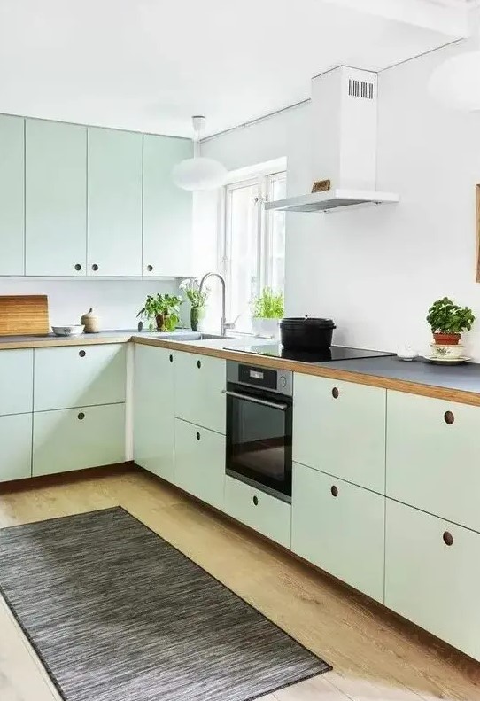 a mint green Scandinavian kitchen with MDF cabinets, black countertops and a white backsplash, a dark rug and built-in appliances