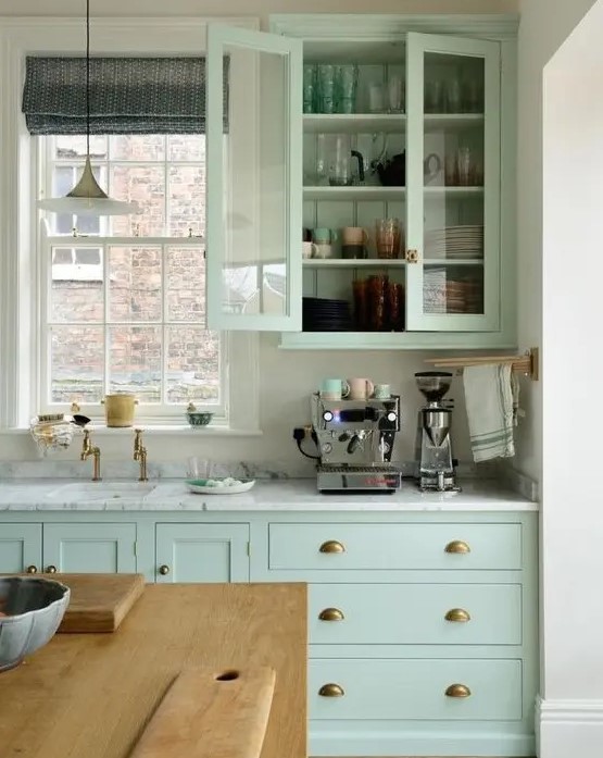 a mint green kitchen with white stone countertops, brass handles, a window to bring some natural light in