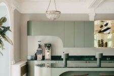 a modern and very refined sage green kitchen with curved cabinetry, a sculptural kitchen island and dark green countertops