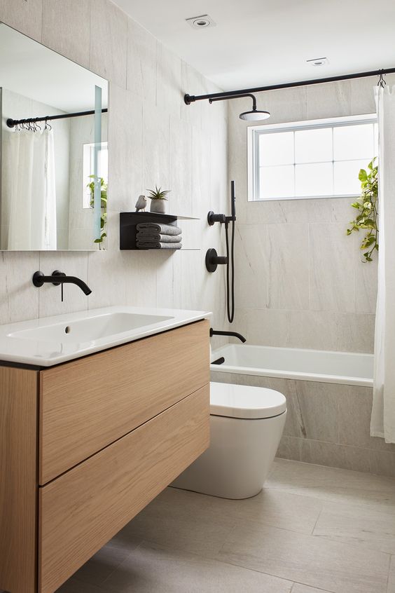 a modern bathroom with neutral large format tiles, a timber vanity, black fixtures, greenery, a mirror cabinet