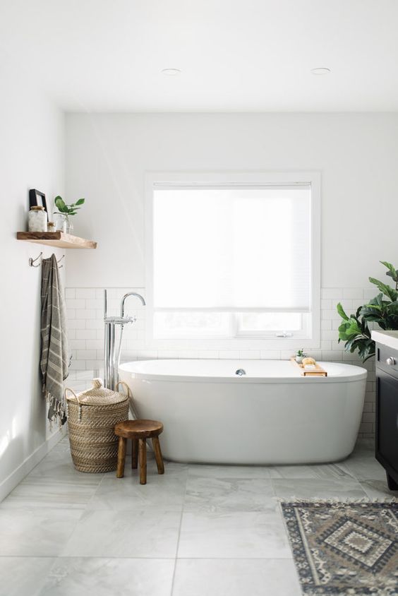 a modern bathroom with white subway and stone large format tiles, an oval tub, a black vanity, some baskets and a stool
