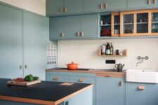 a modern egg blue kitchen with black countertops and a white square tile backsplash, a black lamp is stylish