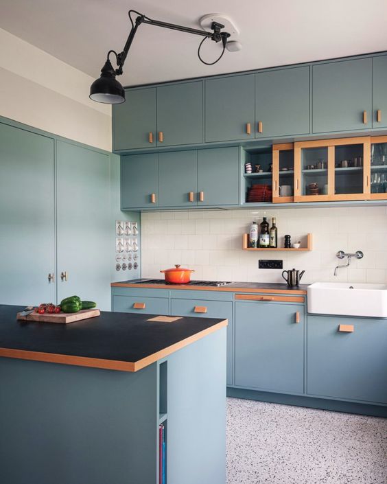 a modern egg blue kitchen with black countertops and a white square tile backsplash, a black lamp is stylish