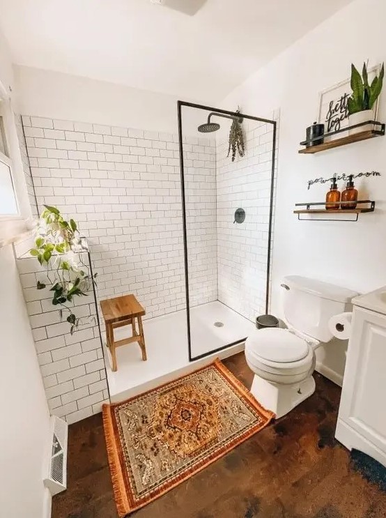 a modern farmhouse bathroom with white subway tiles, a wooden floor, white furniture, potted greenery and a boho rug