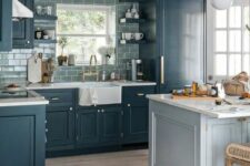 a modern farmhouse kitchen with navy shaker cabients, a grey subway tile backsplash, a pale blue kitchen island, a lamp on chain