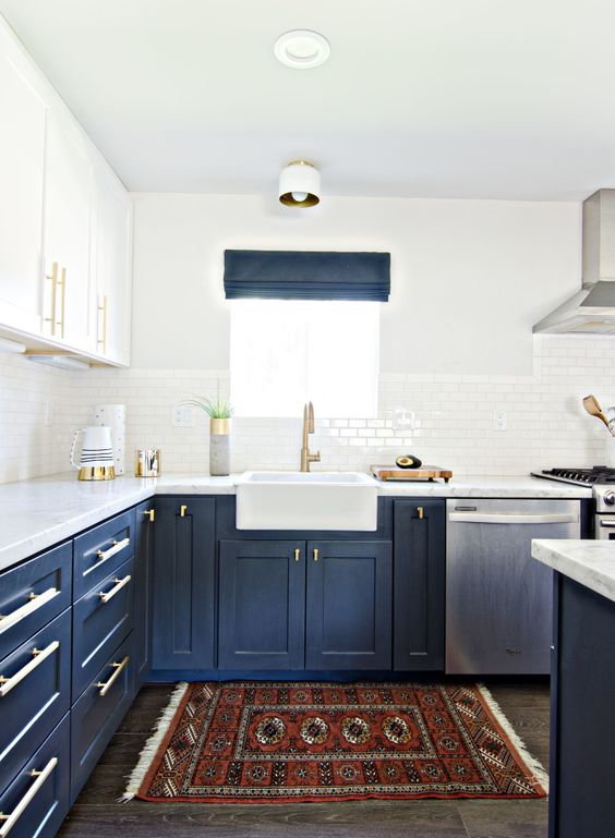 a modern farmhouse kitchen with white upper and navy lower cabinets, white tiles, a boho rug and white stone countertops