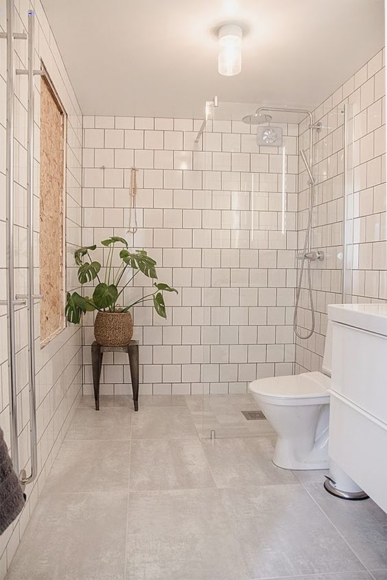 a modern neutral bathroom with white square and large format tiles, a white vanity, a stool with a potted plant and some lights