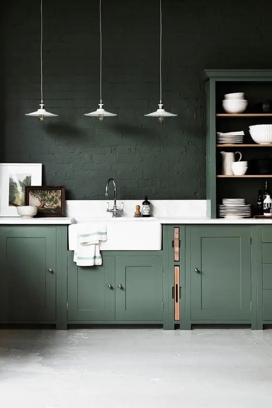 a moody hunter green kitchen with vintage cabinets, dark green brick walls, a white stone backsplash and countertops