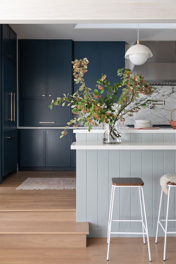 a navy kitchen with a dove grey shiplap kitchen island, white stone countertops and pendant lamps, a white marble backsplash