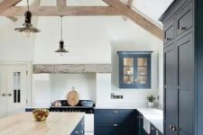a navy kitchen with a white backsplash, countertops, a large island with a wooden countertop and wooden beams