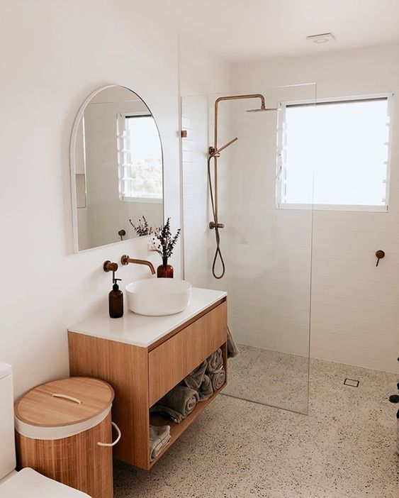a neutral bathroom with a shower space, a stained vanity, a wooden can with a lid and some decor