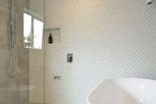 a neutral bathroom with mismatching tiles, an oval tub, a grey tile accent wall, pendant porcelain pendant lamps
