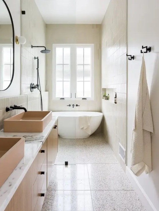 a neutral bathroom with tiles cladding the walls and floor, an oval tub, a floating vanity with tan sinks and black fixtures