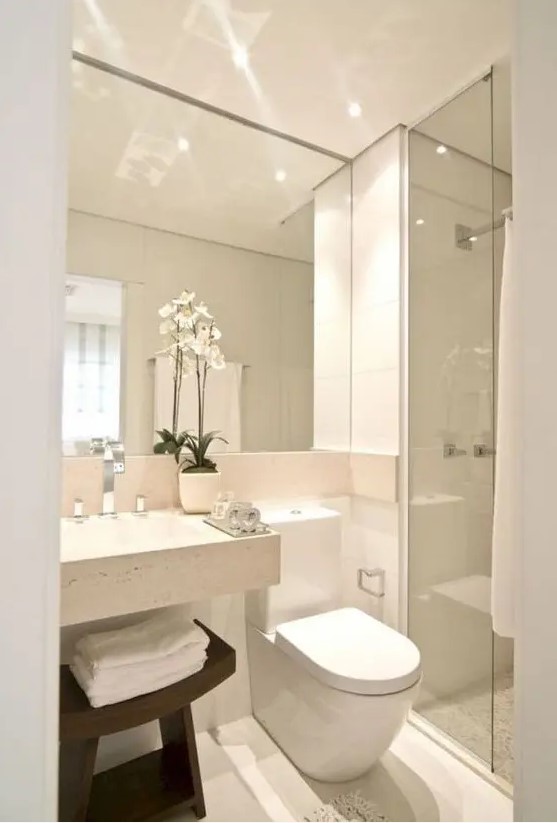 a neutral minimalist bathroom with a large mirror, a square sink, a shower space and a dark stained wooden stool