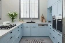 a pastel blue farmhouse kitchen with shaker cabinets, white stone countertops, black handles, built-in appliances