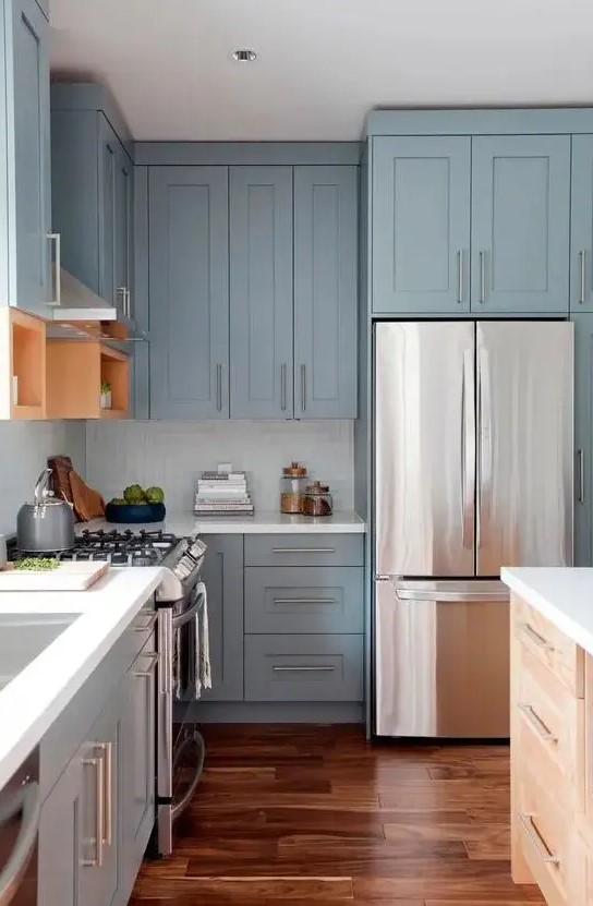 a pastel blue shaker style kitchen with a white square tile backsplash, white countertops and stainless steel handles is super chic and airy