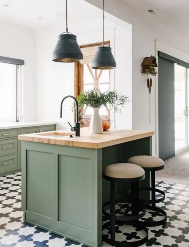a pretty sage green kitchen with shaker cabinets, a small kitchen island, stone and butcherblock countertops and black pendant lamps
