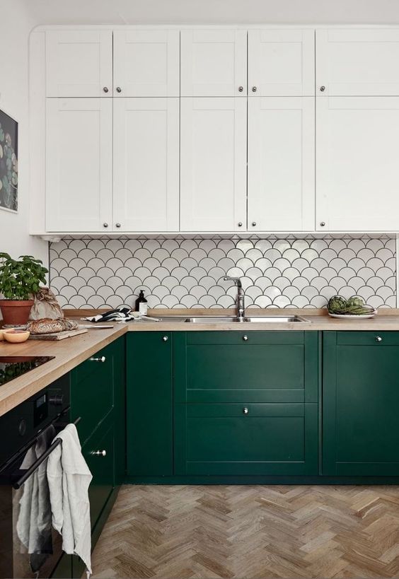 a refined kitchen with forest green and white cabinets, a fishscale tile backsplash and butcherblock countertops is cool