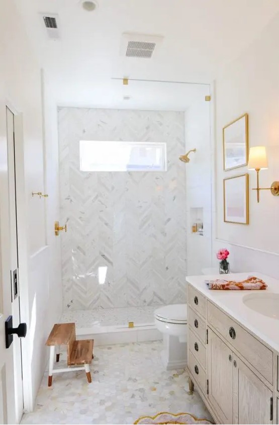 a refined neutral bathroom with herringbone and marble tiles, a shower space, a stained vanity and gold fixtures