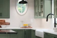 a refined olive green kitchen with glass and shaker cabinets, white and black countertops, a white scale tile backsplash and black handles