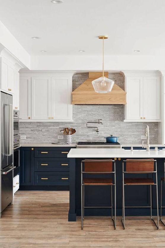 a refined two-tone kitchen with white and navy shaker cabinets, a grey tile backsplash, leather chairs and a pendant lamp