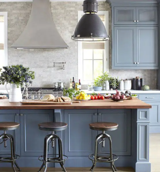 a refined vintage kitchen with a grey tile backsplash and countertops, blue shaker style cabinets, industrial stools and pendant lamps