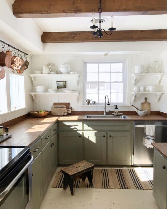 a relaxed farmhouse kitchen with white shiplap walls, light green cabinets, butcherblock countertops, wooden beams