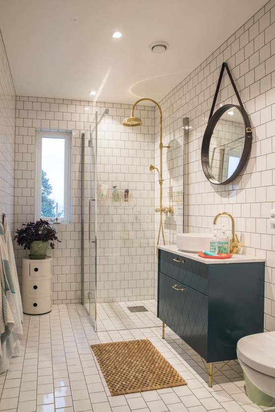 a small and bright bathroom with white tiles, a navy vanity, a side table with a plant and touches of gold here and there
