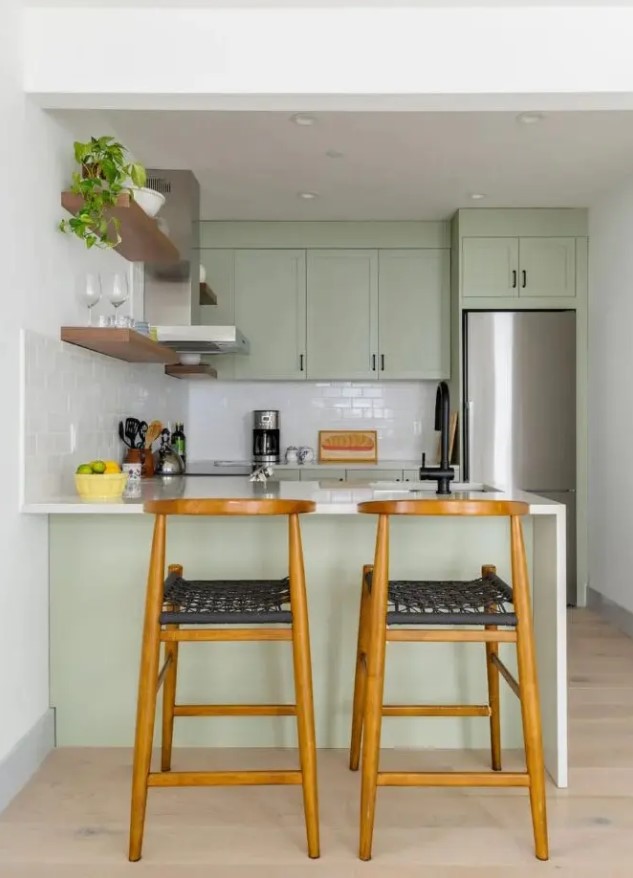 a small and cool sage green kitchen with shaker cabinets, white stone countertops and a white subway tile backsplash, black handles for a modern touch