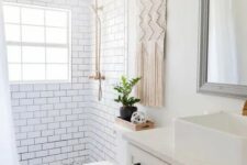 a small and neutral boho bathoom with white subway tiles and black and white ones, a farmhouse vanity, a macrame hanging and touches of black