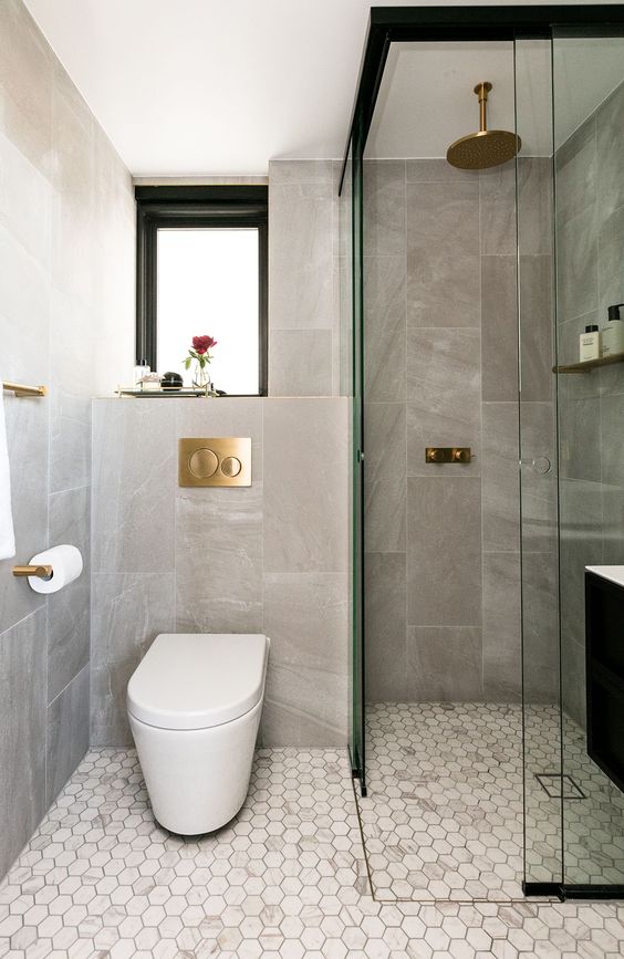 a small and stylish bathroom with hex tiles, a shower space, a black vanity, brass and gold fixtures is cool