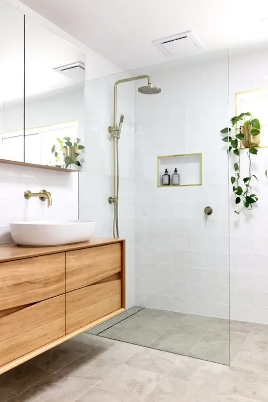 a small and welcoming modern bathroom with white and grey tiles, a catchy wooden vanity, a mirror cabinet and touches of brass