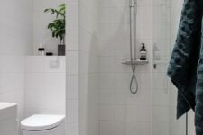 a small bathroom with a shower separate with white long tiles, a printed tile floor, a potted plant and a white vanity
