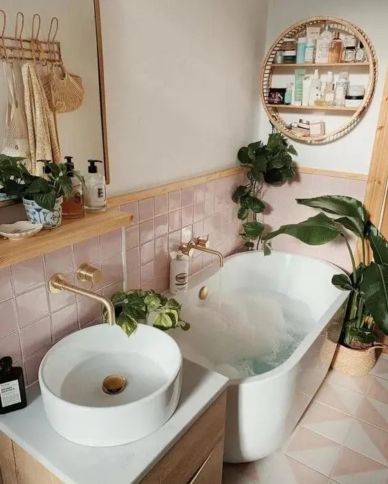 a small boho bathroom with pink tiles, an oval tub, a vanity with a sink, some potted plants and a shelf