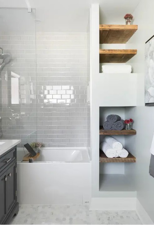 a small contemporary bathroom with white herringbone and black and white tiles, a tub and a floating timber vanity