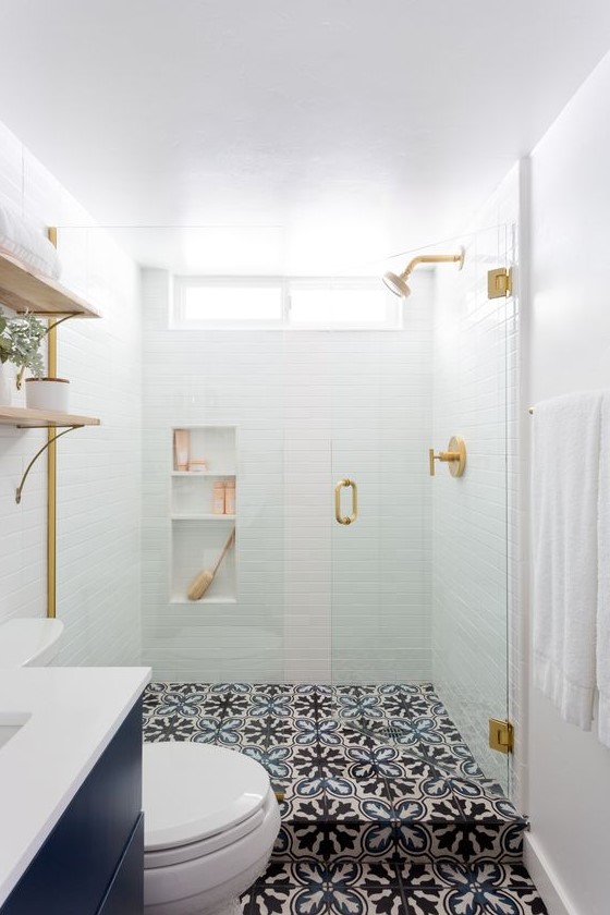 a small contemporary bathroom with white tiles in the shower, patterned tile floor, a navy vanity and touches of gold