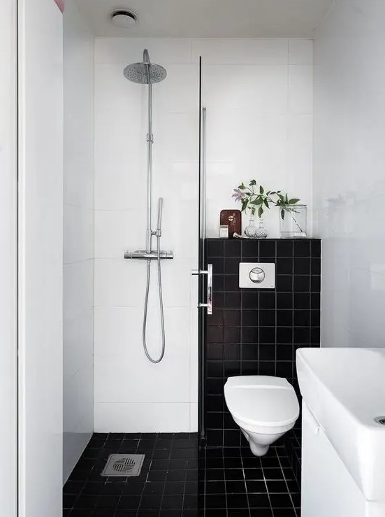 a small contrasting bathroom with black and white tiles, a shower space, a sink and greenery to refresh the look