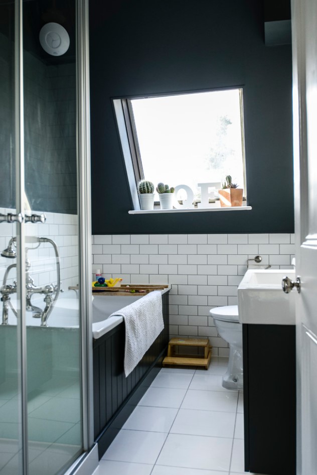 a small elegant attic bathroom with white subway tiles, a black clad bathtub and vanity, a white tub and sink
