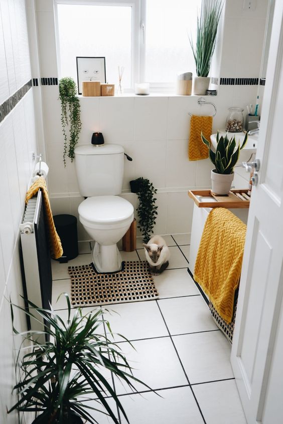 a small modern bathroom with a tub and a shelf, a wall-mounted sink, potted greenery and yellow towels is super cool