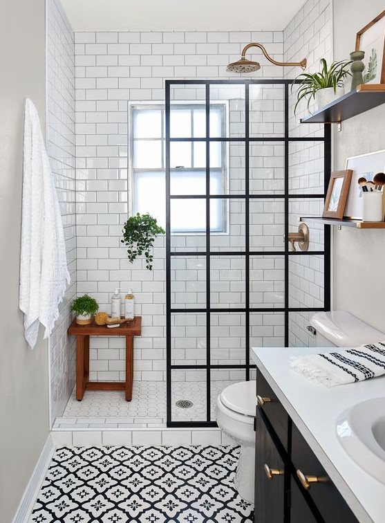 a small monochromatic bathroom clad with printed and white subway tiles, a black vanity, a black framed glass divider and brass touches