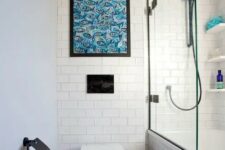 a small neutral bathroom with black and white and white subway tiles, a bathtub and a bold fish artwork
