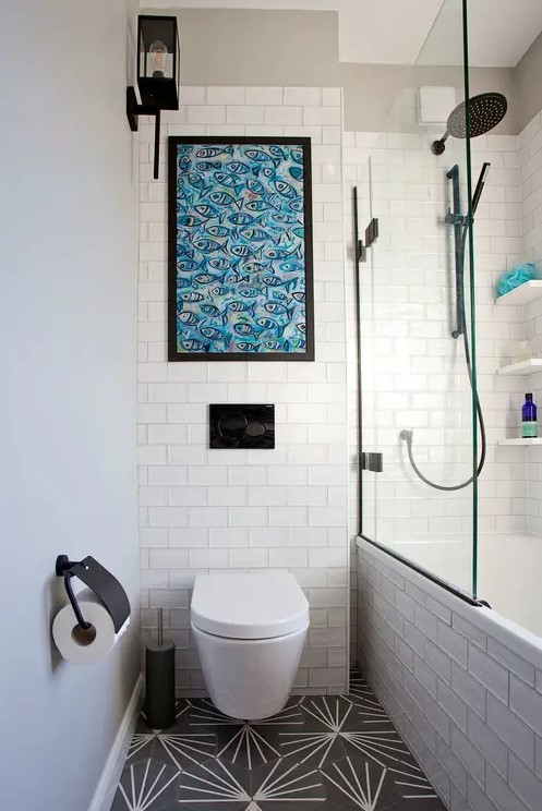a small neutral bathroom with black and white and white subway tiles, a bathtub and a bold fish artwork