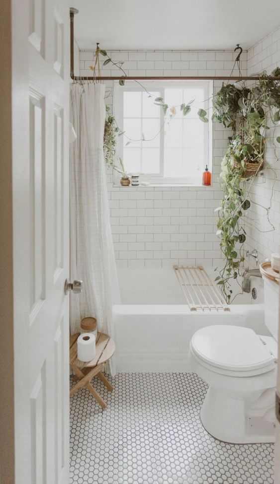 a small neutral boho bathroom clad with white subway and penny tiles, a bathtub, a toilet, some potted greenery and a curtain